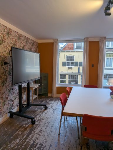 Moderne vergaderruimte met een grote tv en een tafel omringd door rode stoelen.